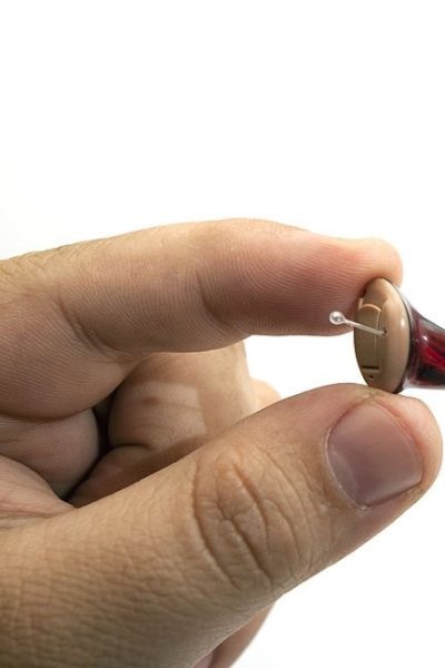 A small red hearing aid being held in a studio setting.